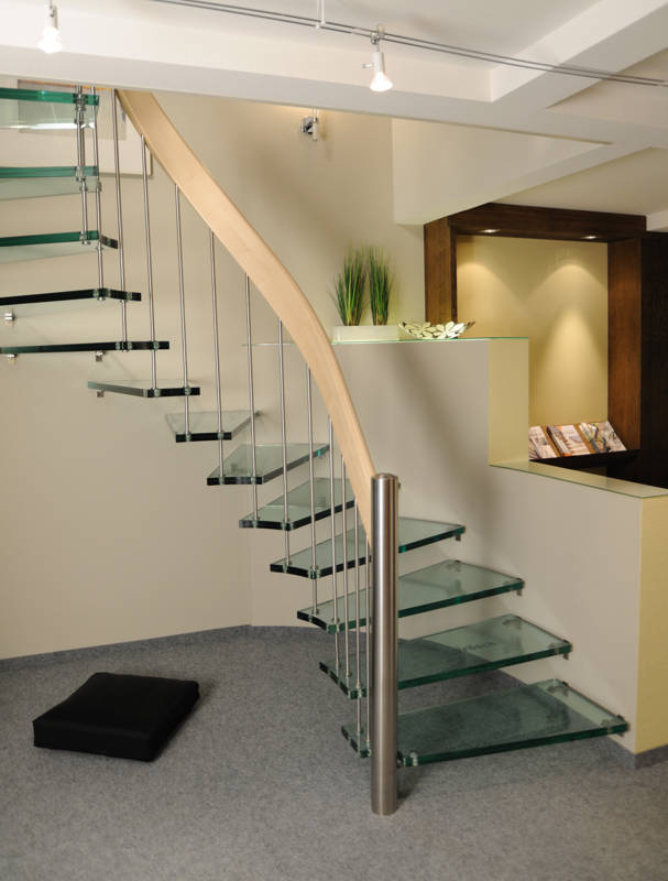 Escalier autoportant courbe avec marches en verre (VSG 31 mm), rampe avec main courante courbe en érable lamellé collé, balustres et poteau de départ en inox. 