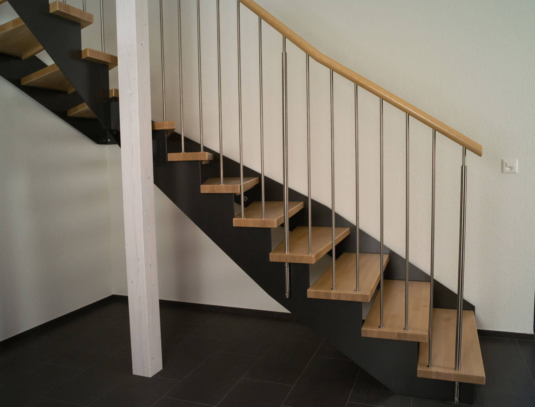 Limon métal découpé en crémaillère côté jour avec fixation des marches sur le dessus et fixation contre le limon côté mur. Balustres inox fixés sur les marches et à la main courante.