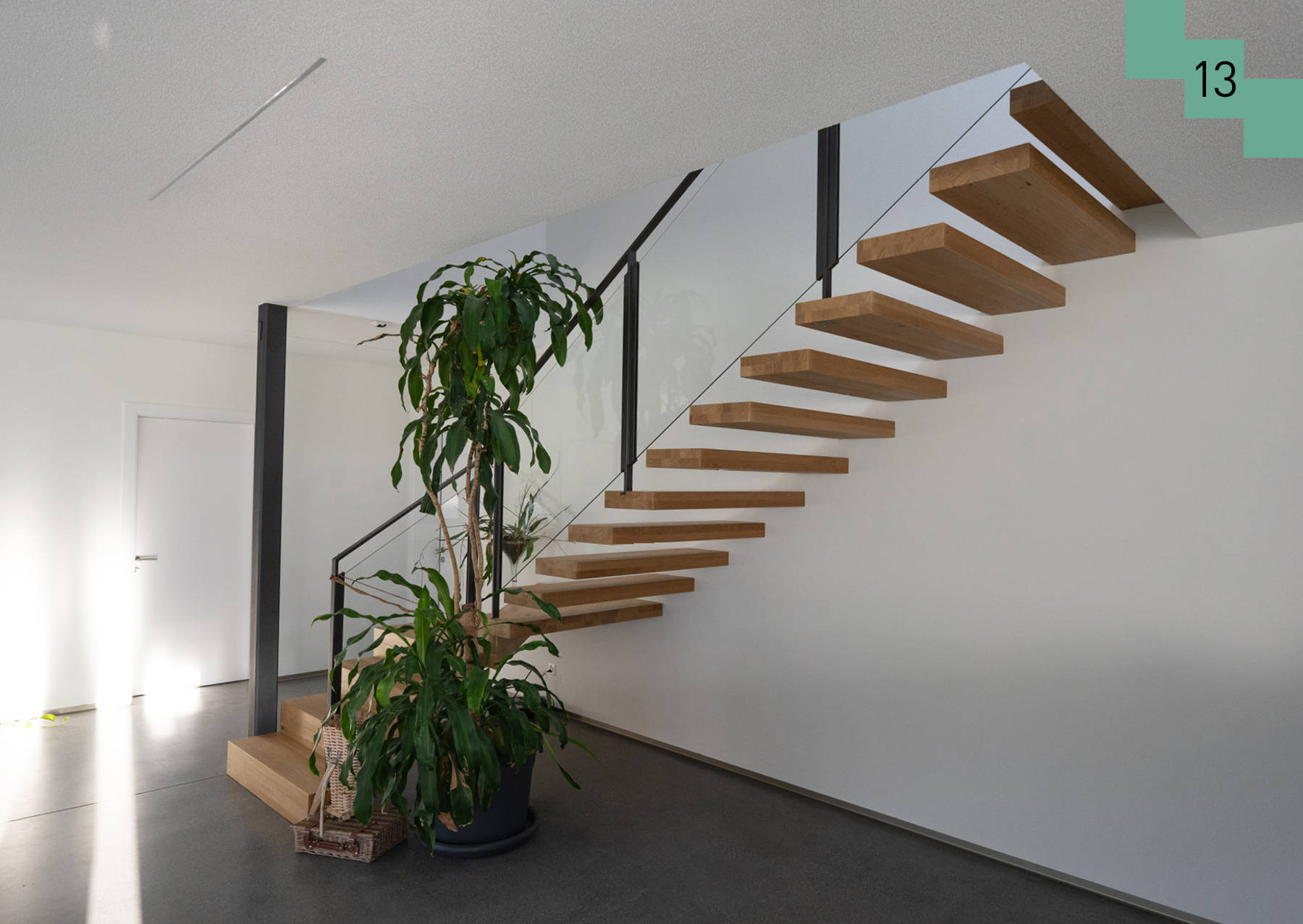 Stufen in Eiche aus Wand. Geländer mit schwarze Stahlpfosten und Glasfüllungen. 