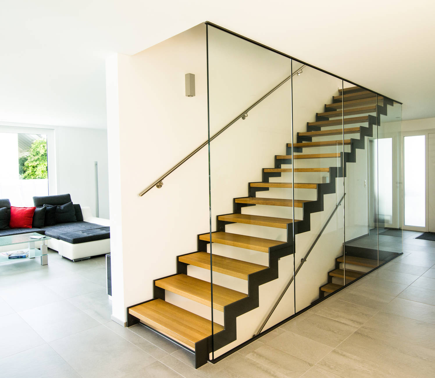 Metallwangentreppe mit beidseitig abgetreppten Wangen und Massivholzstufen. Lichtseitig raumhohe Verglasung, wandseitig CNS-Handlauf an Wand.