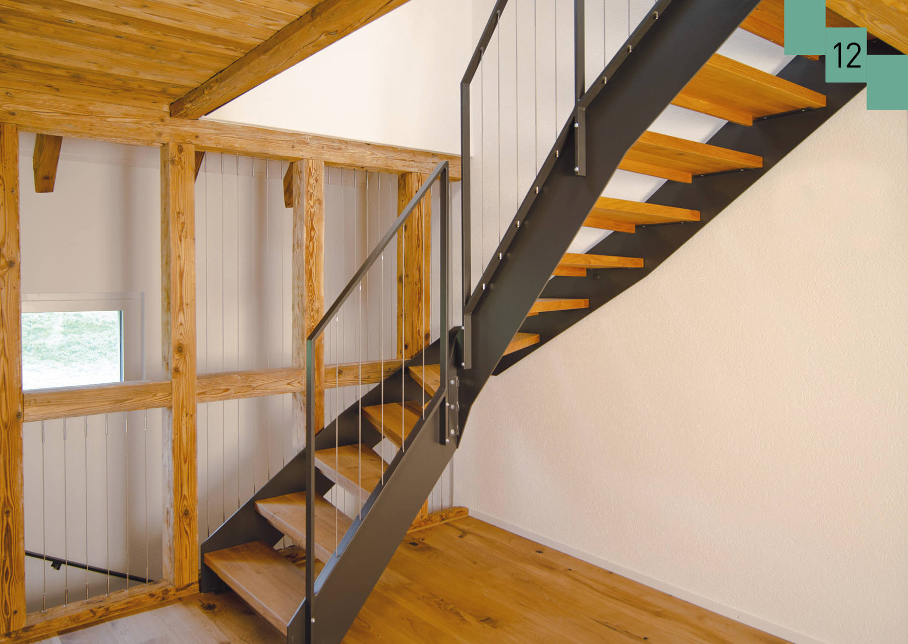 Metallwangentreppe mit Eichenstufen. Metallgeländer mit senkrechten Chromstahlseilen. Die Seile wurden auch zur Absturzsicherung in die bestehenden Balken montiert. 