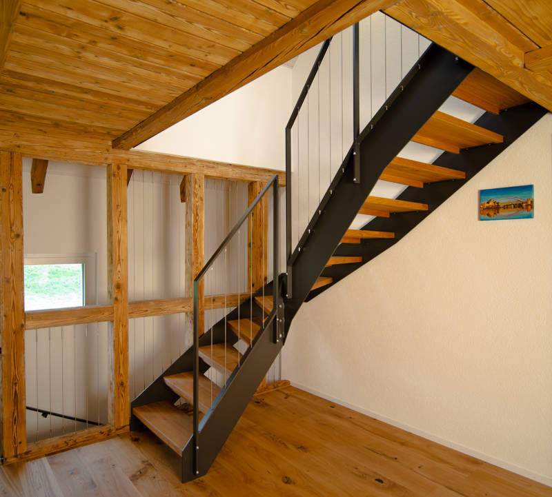Metallwangentreppe mit Massivholzstufen in Eiche. Geländer mit vertikalen Inox-Seilen.