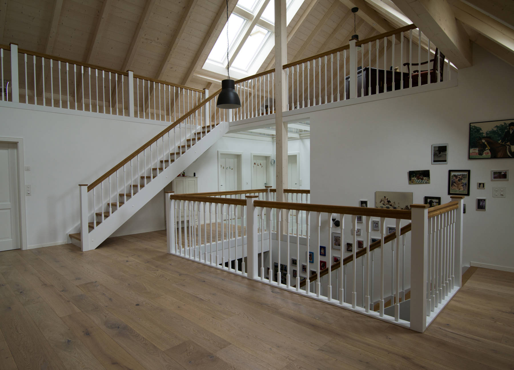Holzwangentreppe mit Holzgeländer. Vertikale Holzsprossen zwischen Handlauf und Wange montiert. Wangen, Futterbretter, Sprossen, Pfosten und Bodenleiste weiss deckend lackiert. Stufen, Handlauf und Pfostenkopf in Eiche natur geölt.