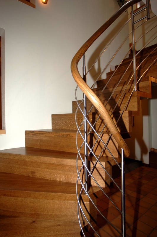 Escalier Linéa en chêne rustique huilé sombre, fixé au mur. Courbe au départ. Rampe type Reling inox, main courante bois.