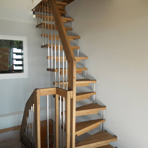 Escalier autoportant avec marches trapézoïdales en chêne. Balustrade avec barreaux carrés.