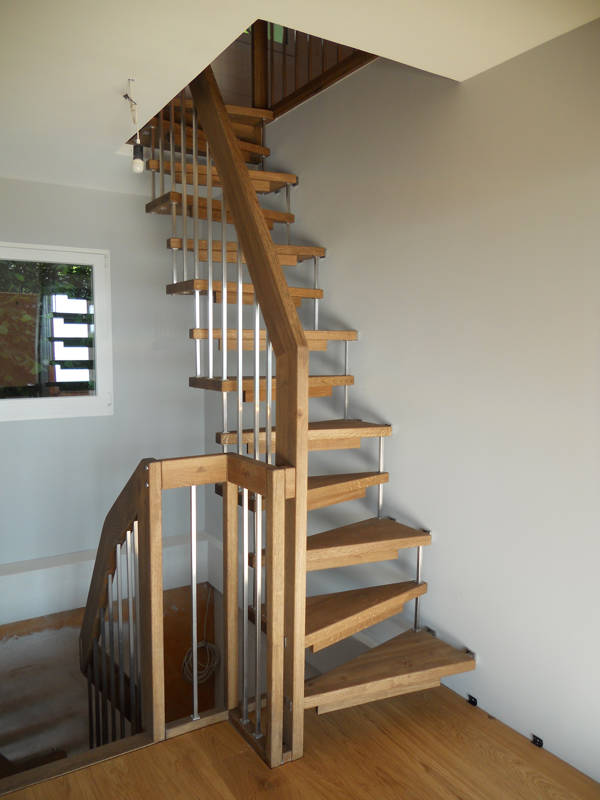 Escalier autoportant avec marches trapézoïdales en chêne. Balustrade avec barreaux carrés.