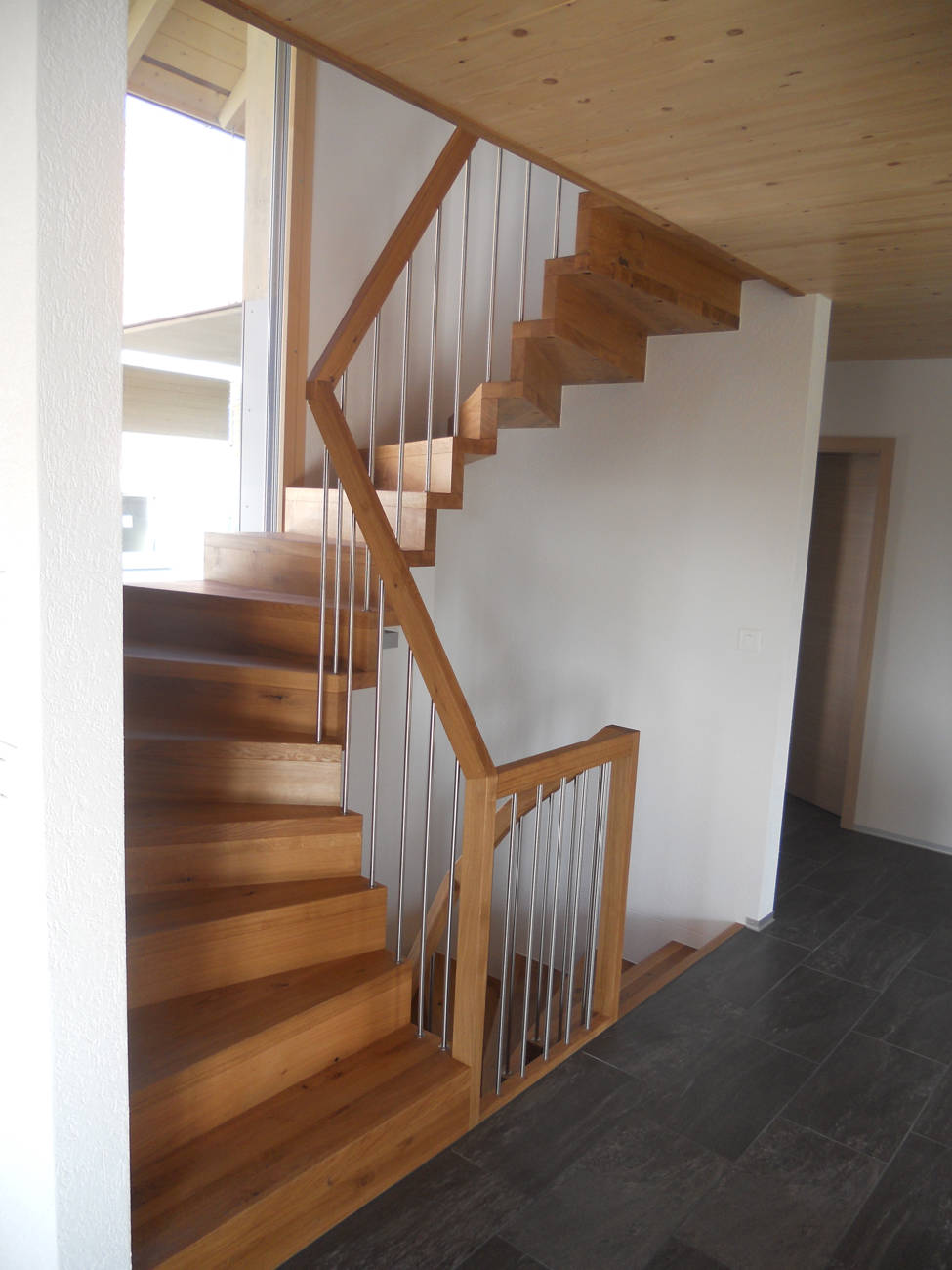 Treppe aus Eiche, natur geölt, mit der Wand verschraubt. Geländer mit vertikalen Edelstahlsprossen und Holzhandlauf.