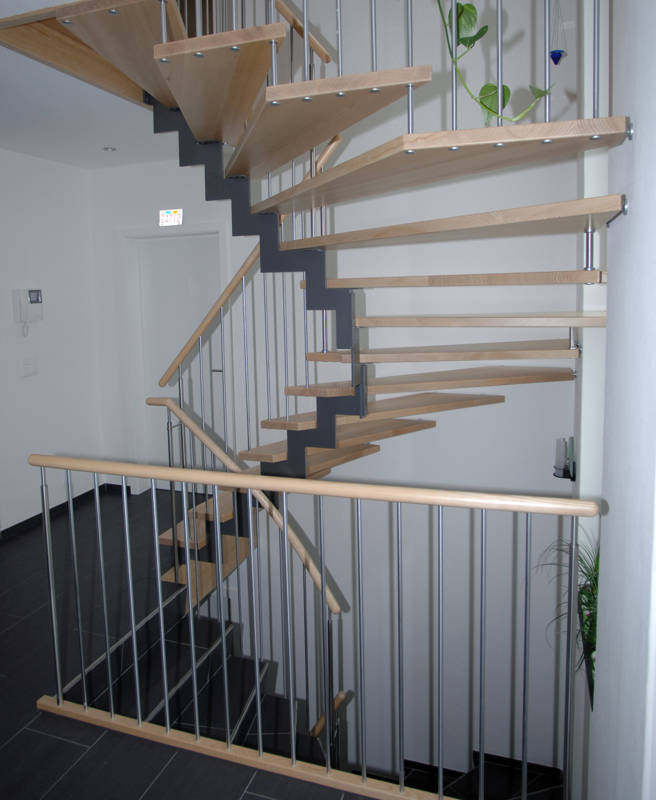 Stufen innen auf abgetrepptem Metallholmen aufgesattelt, aussen direkt in der Wand befestigt. Treppengeländer mit Edelstahlsprossen und rundem Holzhandlauf.