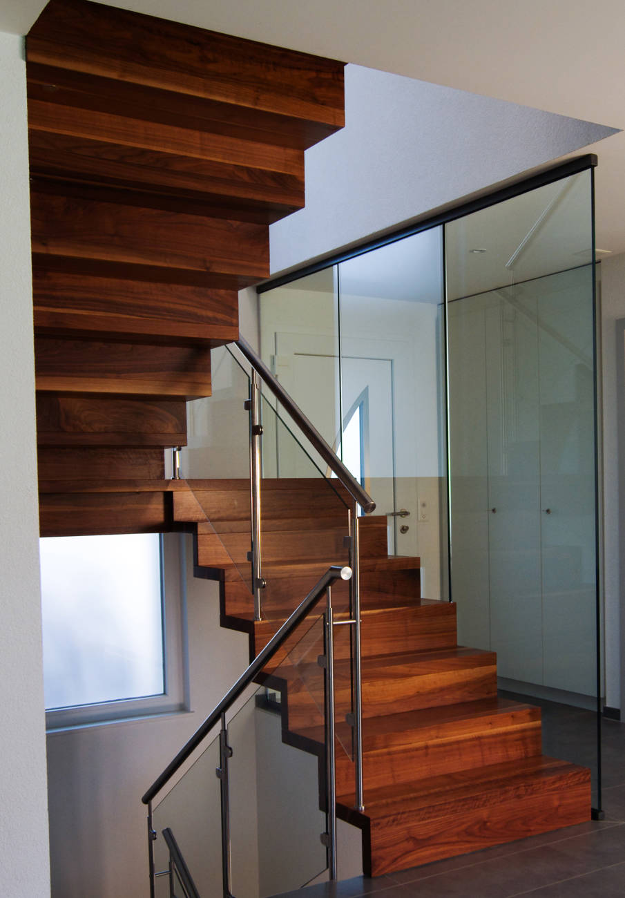 Faltwerktreppe mit Podest in amerikanischem Nussbaum natur farblos lackiert. 1. Lauf mit Metallsattel (sieht man auf Bild nicht) und 2. Lauf mit der Wand verschraubt. Relinggeländer aus Edelstahl und CNS-Handlauf. Glaswand raumhoch.