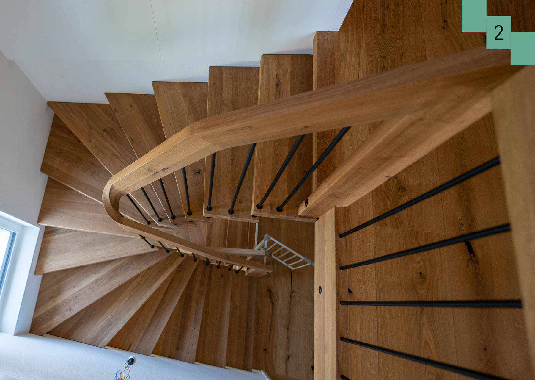 Freitragende Treppe in Eiche. Handlauf mit Krümmling und schwarzen Sprossen.