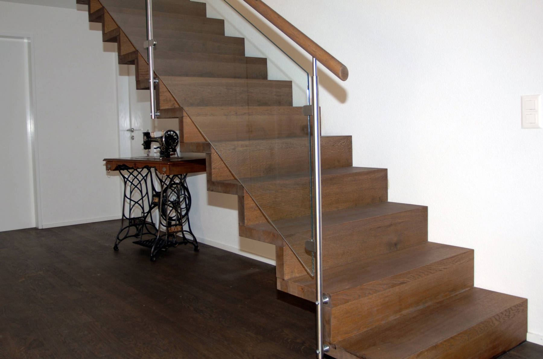 Faltwerktreppe aus Eiche dunkel geölt, mit der Wand verschraubt. Geländer mit Edelstahlpfosten, Holzhandlauf und Glasfüllungen.