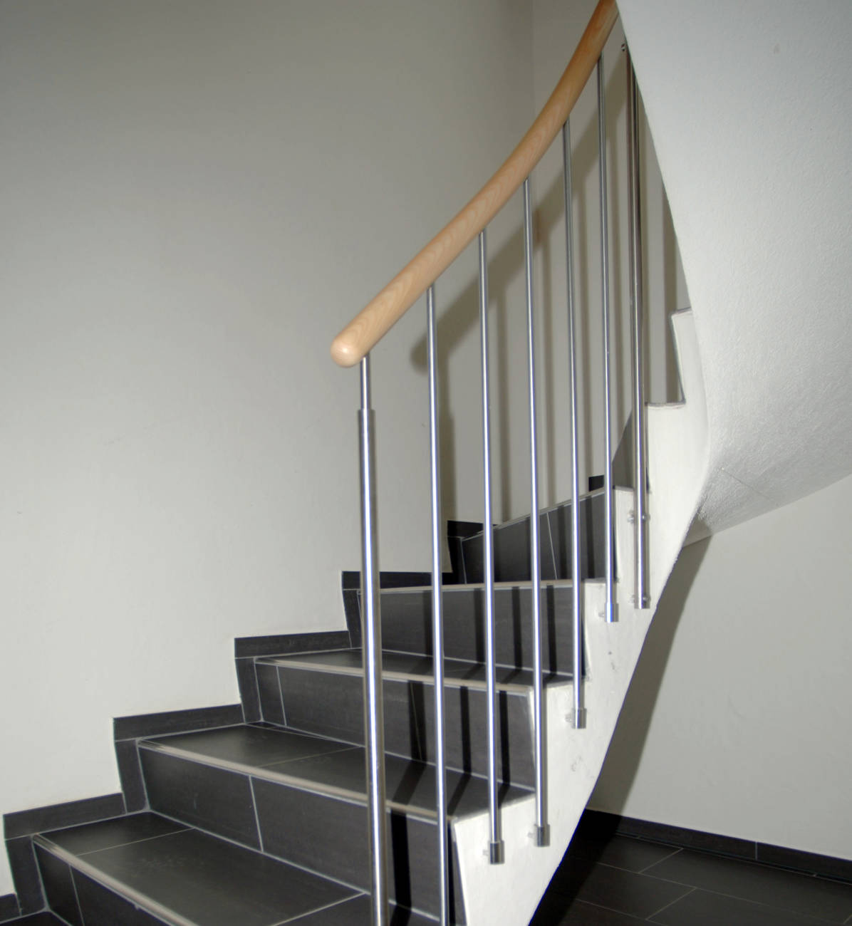 Edelstahlsprossen mit speziellem Sprossenschuh seitlich an Betontreppe befestigt. Rundstabhandlauf aus Holz.