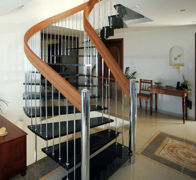 Freitragende Bogentreppe mit Glasstufen und beidseitigem Geländer. Handlauf aus Nussbaum, Geländersprossen und Pfosten glanz chrom.