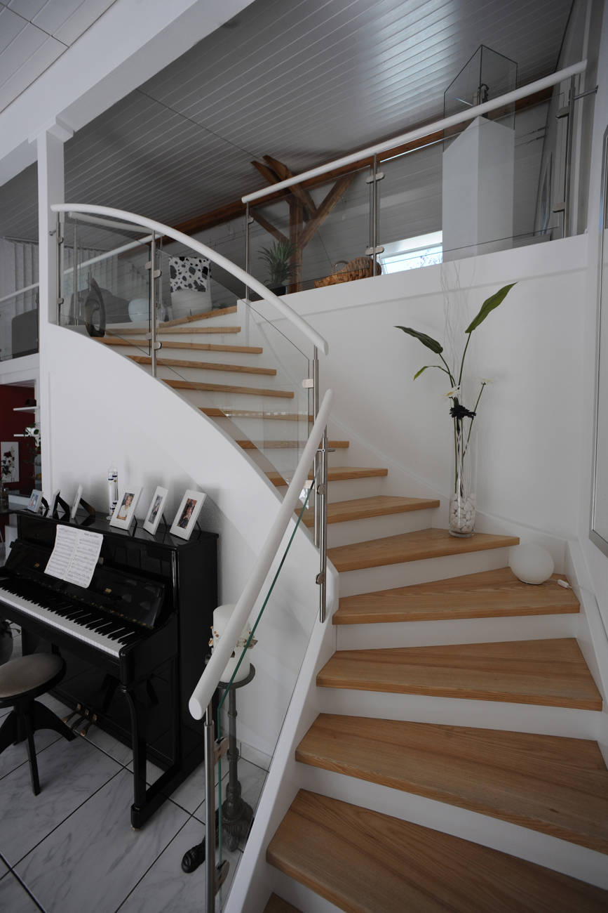 Geschlossene Holzwangentreppe. Wangen, Futterbretter und Handlauf deckend weiss versiegelt. Geländer aus Edelstahlpfosten mit Verbundsicherheitsglas.