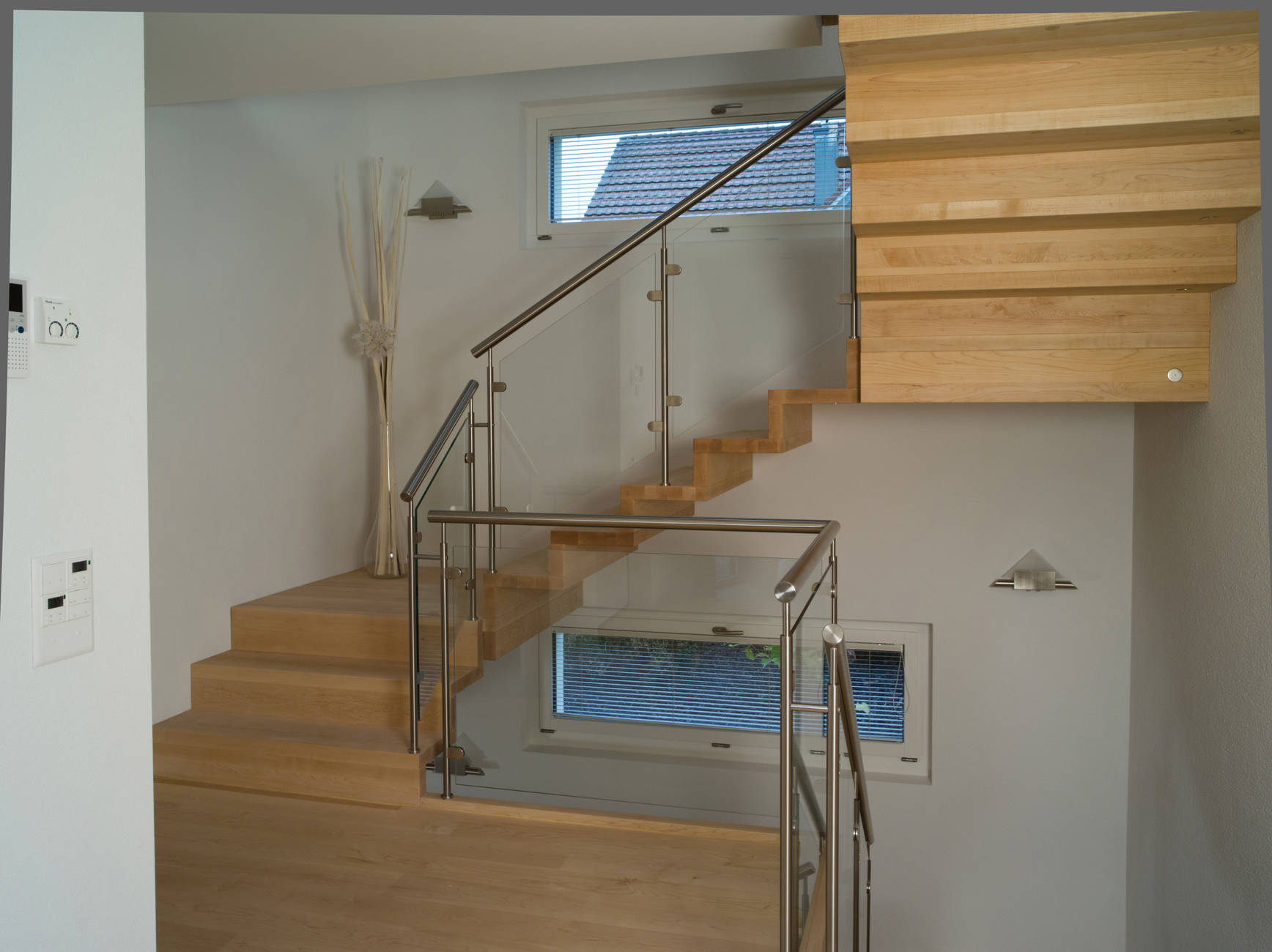 Faltwerktreppe aus kanadischem Ahorn natur geölt, mit der Wand verschraubt. Geländer mit Edelstahlpfosten, CNS-Handlauf und Glasfüllungen.