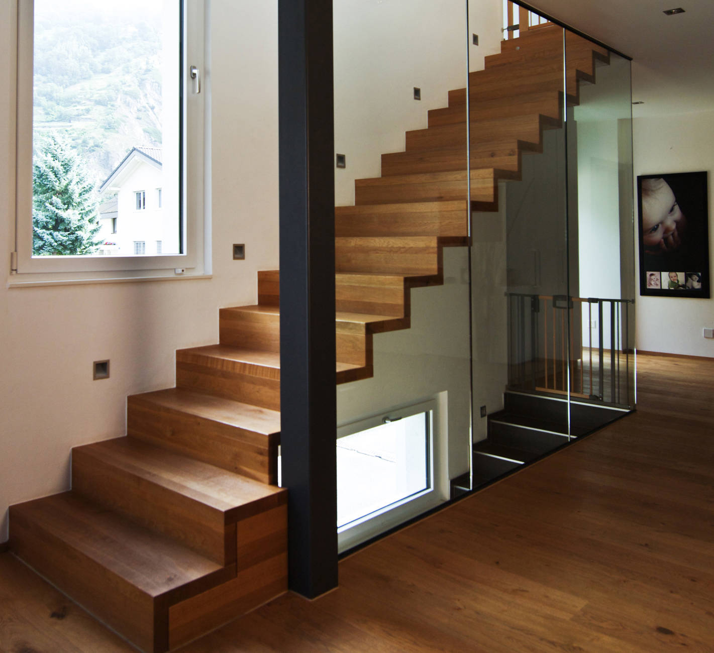 Faltwerktreppe in Chêne Bourgogne (Eiche mit Ästen) geölt, mit der Wand verschraubt. Glaswände von Boden bis Unterkant Decke in Metallkonstruktionen montiert.